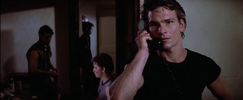 Movie still from “The Outsiders” (1983), directed by Francis Ford Coppola – A man on a cell phone in front of another man; Close Up shot, Over the shoulder angle