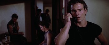 Movie still from “The Outsiders” (1983), directed by Francis Ford Coppola – A man talking on a phone while another man looks on; Close Up shot, Over the shoulder angle