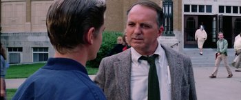 Movie still from “The Outsiders” (1983), directed by Francis Ford Coppola – A man wearing a suit and tie talking to another man; Medium shot, Over the shoulder angle