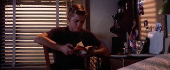 Movie still from “The Outsiders” (1983), directed by Francis Ford Coppola – A man sitting at a table holding a book; Medium shot, Over the shoulder angle