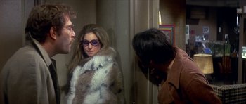 Movie still from “The Owl and the Pussycat” (1970), directed by Herbert Ross – A woman wearing a fur coat standing next to two other people; Medium shot, Over the shoulder angle