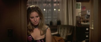 Movie still from “The Owl and the Pussycat” (1970), directed by Herbert Ross – A woman sitting in front of a couch in a room; Close Up shot, Over the shoulder angle