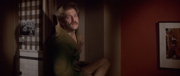 Movie still from “The Owl and the Pussycat” (1970), directed by Herbert Ross – A man sitting on a chair in a room; Medium shot, Low angle
