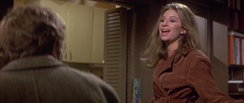 Movie still from “The Owl and the Pussycat” (1970), directed by Herbert Ross – A woman in a brown bathrobe is smiling; Medium shot, Over the shoulder angle