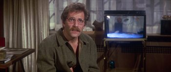 Movie still from “The Owl and the Pussycat” (1970), directed by Herbert Ross – A man with a beard and glasses sitting in front of a television; Close Up shot, Over the shoulder angle