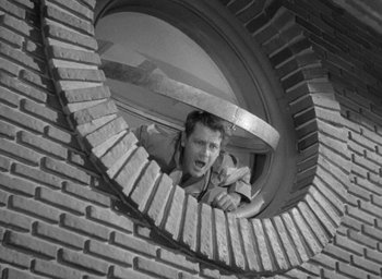 Movie still from “The Palm Beach Story” (1942), directed by Preston Sturges – A black - and - white photo of a man looking through a round window; Medium shot, Low angle