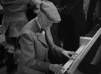 Movie still from “The Palm Beach Story” (1942), directed by Preston Sturges – An older man playing a piano in a crowd; Medium shot, High angle