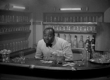 Movie still from “The Palm Beach Story” (1942), directed by Preston Sturges – A man sitting at a bar in front of a bunch of bottles; Medium shot, High angle