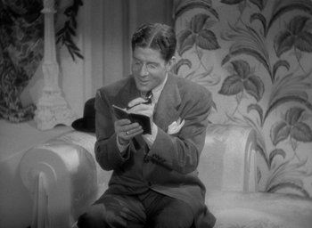 Movie still from “The Palm Beach Story” (1942), directed by Preston Sturges – A black and white photo of a man reading a book; Medium shot, High angle
