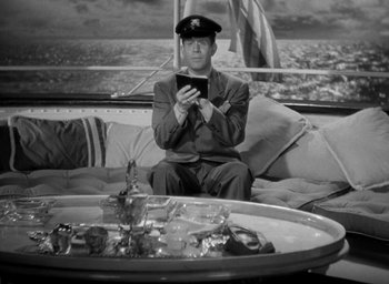 Movie still from “The Palm Beach Story” (1942), directed by Preston Sturges – A man sitting on top of a couch looking at a tablet; Medium shot, High angle