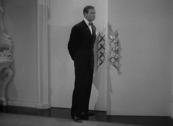 Movie still from “The Palm Beach Story” (1942), directed by Preston Sturges – A black and white photo of a man standing in front of an open door; Medium shot, High angle