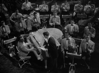 Movie still from “The Palm Beach Story” (1942), directed by Preston Sturges – An old photo of a man playing the piano in front of an orchestra; Extreme Wide shot, High angle