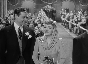 Movie still from “The Palm Beach Story” (1942), directed by Preston Sturges – A man and a woman are standing in front of a crowd; Medium shot, High angle
