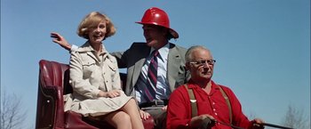 Movie still from “The Parallax View” (1974), directed by Alan J. Pakula – A man in a red hat sitting next to two women; Medium shot, Low angle