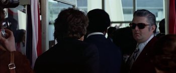 Movie still from “The Parallax View” (1974), directed by Alan J. Pakula – Two men in suits are standing next to each other; Medium shot, Over the shoulder angle