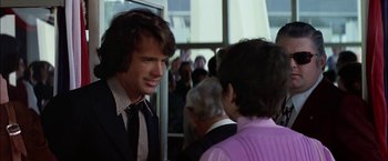 Movie still from “The Parallax View” (1974), directed by Alan J. Pakula – A man in a suit and tie talking to another man in a suit and tie; Medium shot, Over the shoulder angle