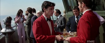 Movie still from “The Parallax View” (1974), directed by Alan J. Pakula – A man in a red jacket is serving drinks to a crowd; Medium shot, Over the shoulder angle