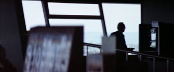Movie still from “The Parallax View” (1974), directed by Alan J. Pakula – A man standing in front of a large window; Medium shot, Over the shoulder angle