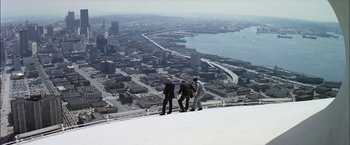 Movie still from “The Parallax View” (1974), directed by Alan J. Pakula – Three men standing on a ledge looking down on a city; Extreme Wide shot, High angle