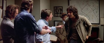 Movie still from “The Parallax View” (1974), directed by Alan J. Pakula – A group of men standing next to each other in a room; Medium shot, Over the shoulder angle