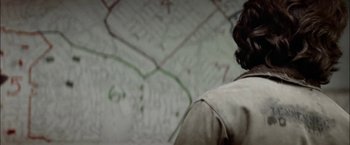 Movie still from “The Parallax View” (1974), directed by Alan J. Pakula – A man standing in front of a wall covered in graffiti; Close Up shot, Over the shoulder angle