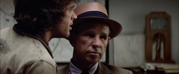 Movie still from “The Parallax View” (1974), directed by Alan J. Pakula – A man wearing a hat talking to another man in a suit; Close Up shot, Over the shoulder angle