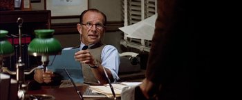 Movie still from “The Parallax View” (1974), directed by Alan J. Pakula – An older man sitting at a table talking to someone; Close Up shot, Over the shoulder angle