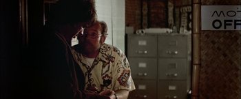 Movie still from “The Parallax View” (1974), directed by Alan J. Pakula – A man and a woman looking at a cell phone in a room; Medium shot, Over the shoulder angle