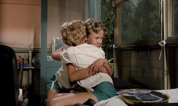 Movie still from “The Parent Trap” (1961), directed by David Swift – Two young children hugging each other in a room; Medium shot, High angle