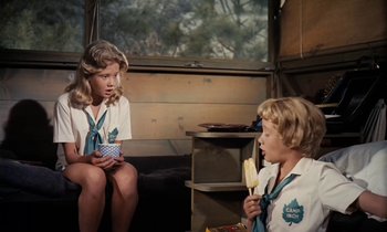 Movie still from “The Parent Trap” (1961), directed by David Swift – Two young girls sitting on a couch in a room; Medium shot, High angle
