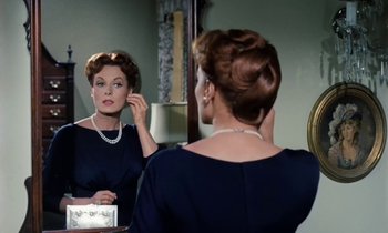 Movie still from “The Parent Trap” (1961), directed by David Swift – A woman looking in the mirror while putting on a pearl necklace; Close Up shot, Over the shoulder angle