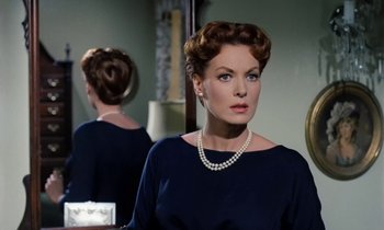 Movie still from “The Parent Trap” (1961), directed by David Swift – A woman in a blue dress and pearls in front of a mirror; Close Up shot, Over the shoulder angle