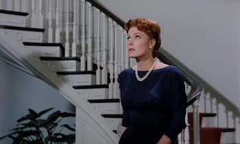 Movie still from “The Parent Trap” (1961), directed by David Swift – A woman in a blue dress standing in front of a staircase; Medium shot, Low angle