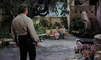 Movie still from “The Parent Trap” (1961), directed by David Swift – An older man standing in front of two women sitting on a bench in a garden; Wide shot, High angle