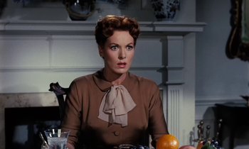 Movie still from “The Parent Trap” (1961), directed by David Swift – A woman sitting at a table with an orange in front of her; Close Up shot, Over the shoulder angle