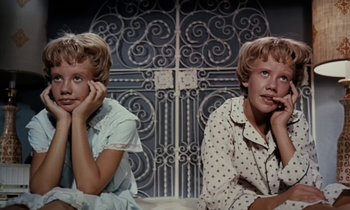 Movie still from “The Parent Trap” (1961), directed by David Swift – Two young women sitting next to each other in front of an iron gate; Close Up shot, Low angle