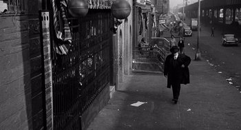 Movie still from “The Pawnbroker” (1964), directed by Sidney Lumet – A man walking down a street past a fence; Wide shot, High angle