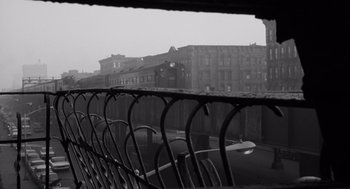 Movie still from “The Pawnbroker” (1964), directed by Sidney Lumet – A black - and - white photo of a fence and buildings in the background; Wide shot, Low angle