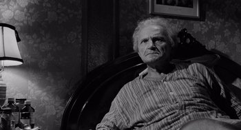 Movie still from “The Pawnbroker” (1964), directed by Sidney Lumet – An older man sitting in a chair in front of a wall; Medium shot, Low angle