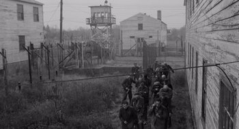 Movie still from “The Pawnbroker” (1964), directed by Sidney Lumet – A group of men standing next to each other near barbed wire fences; Extreme Wide shot, High angle