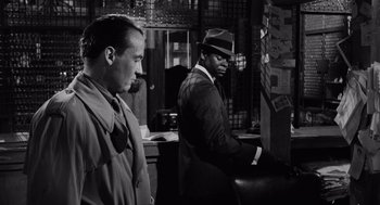 Movie still from “The Pawnbroker” (1964), directed by Sidney Lumet – A man in a hat is standing next to another man in a hat; Medium shot, Over the shoulder angle