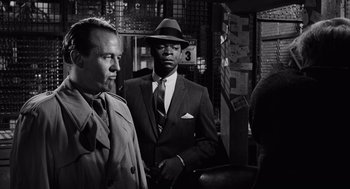 Movie still from “The Pawnbroker” (1964), directed by Sidney Lumet – A black and white photo of a man in a suit and a hat; Medium shot, Over the shoulder angle