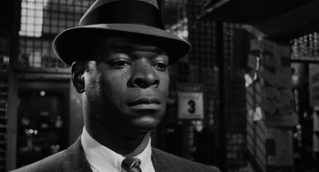 Movie still from “The Pawnbroker” (1964), directed by Sidney Lumet – A black and white photo of a man wearing a suit and a hat; Close Up shot, Over the shoulder angle