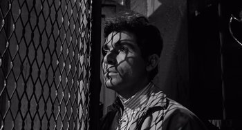 Movie still from “The Pawnbroker” (1964), directed by Sidney Lumet – Black and white photograph of a man looking over a chain link fence; Close Up shot, High angle