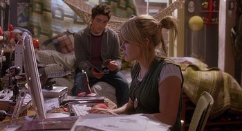 Movie still from “The Perfect Man” (2005), directed by Mark Rosman – A woman sitting at a table with a man in the background; Medium shot, High angle
