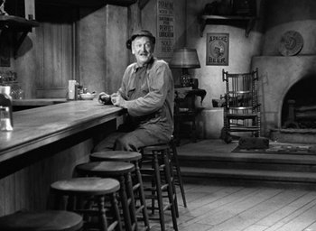 Movie still from “The Petrified Forest” (1936), directed by Archie Mayo – An older man sitting at a bar with a bunch of stools; Wide shot, Low angle