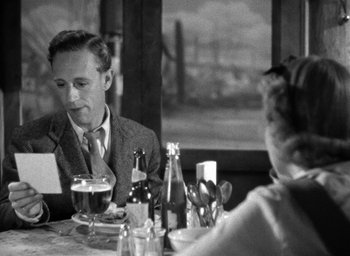 Movie still from “The Petrified Forest” (1936), directed by Archie Mayo – A man sitting at a dinner table with a beer; Medium shot, Over the shoulder angle