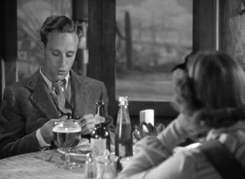 Movie still from “The Petrified Forest” (1936), directed by Archie Mayo – A man sitting at a dinner table with a beer; Medium shot, Over the shoulder angle