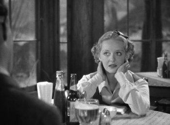 Movie still from “The Petrified Forest” (1936), directed by Archie Mayo – A black and white photo of a woman sitting at a table; Medium shot, Over the shoulder angle