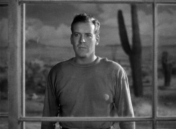 Movie still from “The Petrified Forest” (1936), directed by Archie Mayo – Black and white photograph of a man in front of a cactus; Medium shot, Low angle